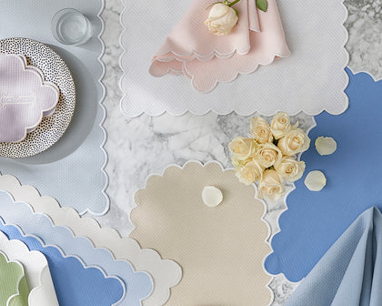 Scalloped-edge Savannah Gardens placemats and napkins in pastel colors on marble with white roses.