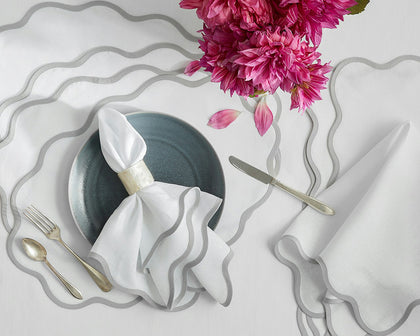 White Scallop Edge placemats and napkins with gray wavy trim, styled with pink dahlias and a dark plate.
