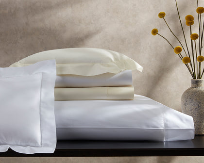 White and cream Sierra Hemstitch bedding stacked on a console beside yellow craspedia blooms.