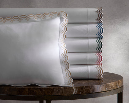 White Stella bedding with scalloped embroidered trim in assorted colors stacked on a marble table.