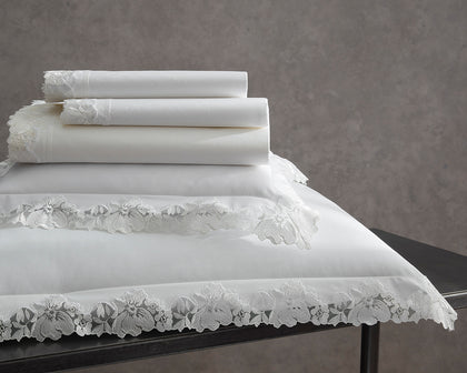 White Virginia bedding with floral lace trim stacked on a dark table.