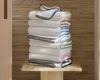 White Whipstitch towels with contrast whipstitch trim in assorted colors stacked on a stone pedestal.