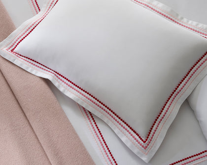White Amara Triple Pearl pillow with red and pink dot-embroidered trim, shown in detail.