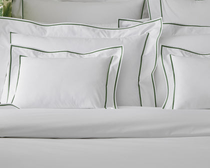 White Ansonia shams with green single-stripe trim, piled on a bed.