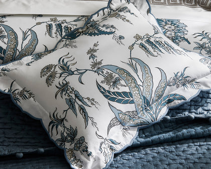 Blue Apolline floral print scalloped pillows on a blue quilted bed.