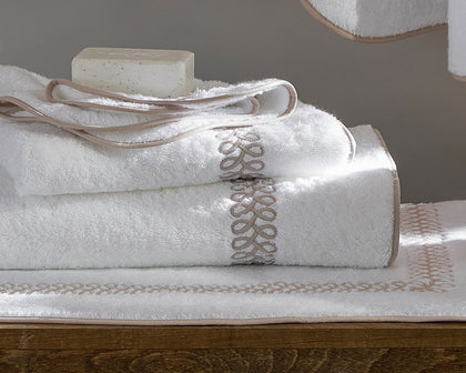 White Astor Braid towels with tan loop-embroidered trim, folded beside a bar of soap.