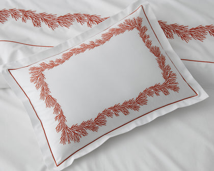 White Atoll pillow with coral-branch embroidered border, styled on a bed.