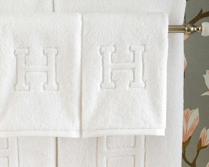 White Auberge towels with a monogrammed letter H in bold relief, hanging on a rod.