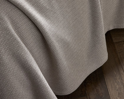 Tan Avalon herringbone-woven blanket draped over a bed.