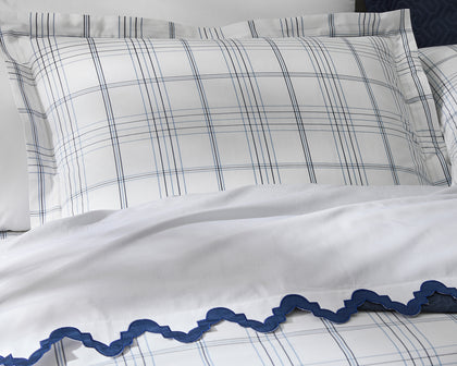 White Aziza bedding with navy wavy trim, styled with plaid pillow shams on top.