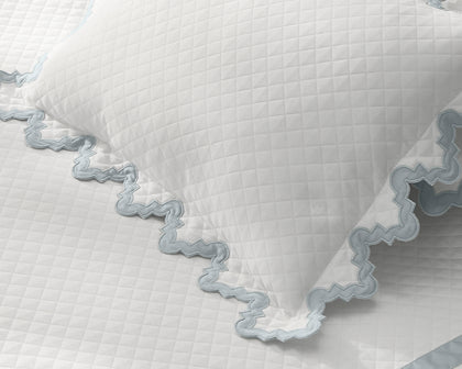White Aziza Matelasse quilted pillow with blue wavy trim.