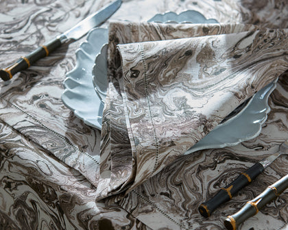 Brown Balthazar marbled-print tablecloth set with scalloped plates and dark handled flatware.
