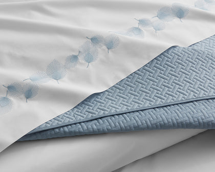Blue Basketweave quilted blanket folded back over white sheets with fan-embroidered trim.