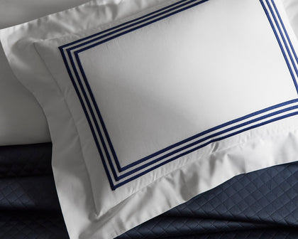 White Bel Tempo pillow with navy triple-stripe trim, styled on a navy quilted bed.