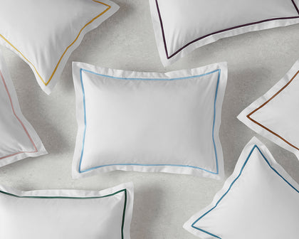 White Bergamo pillows with single-stripe trim in assorted colors, arranged flat.