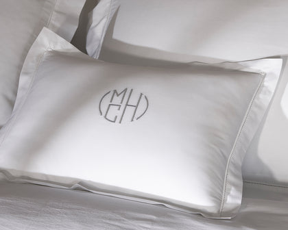 White Bergamo Hemstitch monogrammed pillow with hemstitch trim, styled on a bed.