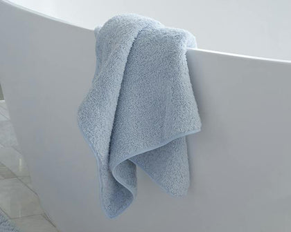 Pale blue Cairo towel draped over the edge of a soaking tub.