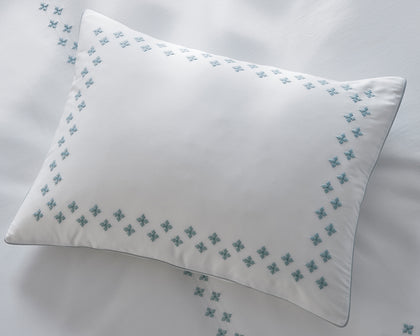 White Casablanca pillow with blue diamond cross-stitch trim, styled on a bed.