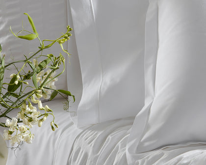 White Ceylon Satin Stitch bedding styled on a bed with white sweet pea flowers.