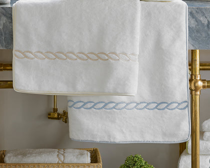 White Classic Chain towels with tan and blue chain-link trim, hung on a brass towel rack.