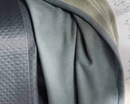 Slate blue Cosmo blanket draped over quilted bedding.