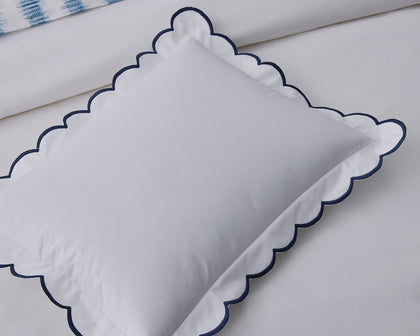 White Dakota scalloped pillow with navy trim, styled on a bed.