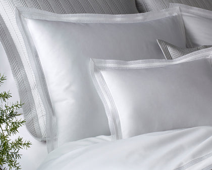 White Grace pillows with lace trimmed borders against a herringbone quilted headboard.