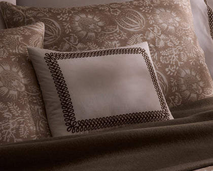 Tan Granada floral print shams with a scroll-embroidered boudoir pillow and a brown throw.