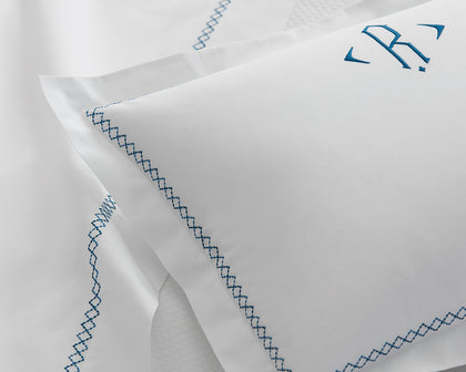 White Hatch monogrammed sham with blue cross-stitch trim, styled on a bed.