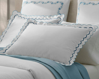 White India scalloped pillows with blue trim, layered with embroidered floral shams and a blue throw.