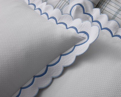 White India Pique scalloped pillow with navy trim, styled on a bed with plaid pillows.