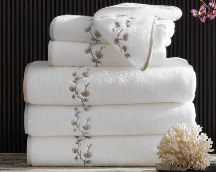 White Jasmine Giza towels with an embroidered floral vine, stacked beside a coral decoration.