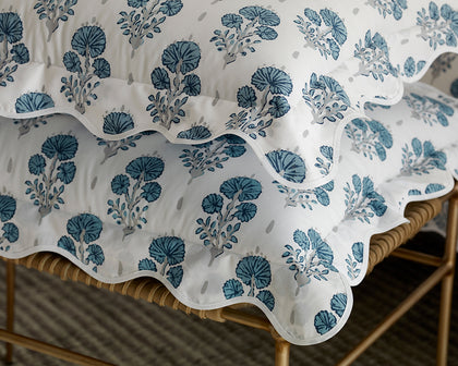 Blue Joplin floral print scalloped pillows stacked on a woven bench.