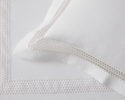 White Lace Pique pillow with a woven lace trim border, styled on a bed.