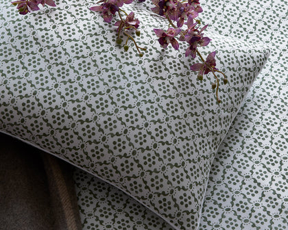 Green Laksha medallion print pillow and sheets, styled on a bed with purple orchids.