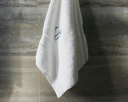 White monogrammed Lotus towel hanging against a marble tile wall.