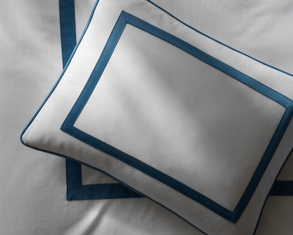 White Louise pillow with a blue bordered trim, styled on a bed.