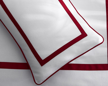 White Louise Pique pillow with a red bordered trim, styled on a bed.