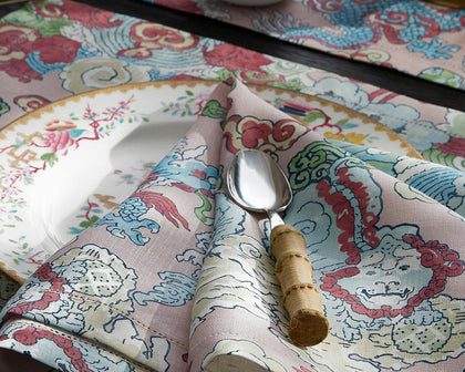 Pink Magic Mountain dragon print placemat and napkin, set with a floral plate and a bamboo-handled spoon.