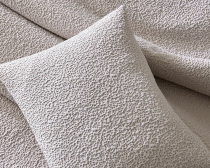 Ivory Malibu textured bouclé pillow and bedding, styled on a bed.
