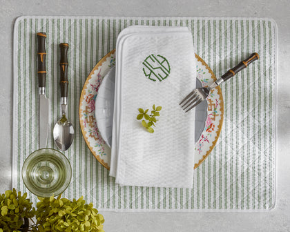 Green-striped Matteo placemat and monogrammed napkin styled with floral china and bamboo-handled flatware.