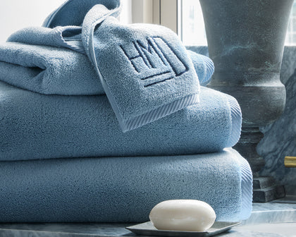 Blue Milagro towels stacked with a monogrammed washcloth on top, beside a soap dish.