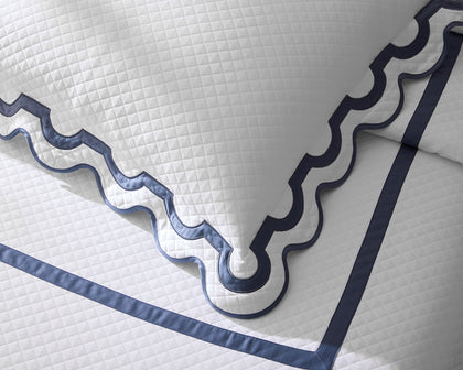 White diamond-quilted Mirasol Matelasse coverlet corner with scalloped navy trim on a bed.