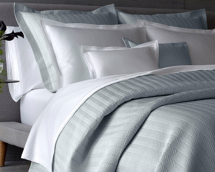 Gray herringbone-quilted Netto bedding styled on a bed with white pillows.