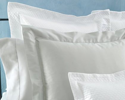 White and gray Nocturne Hemstitch shams layered with quilted pillows on a bed.