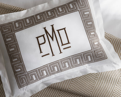 White Ophelia pillow with monogrammed brown Greek key border on herringbone bedding.