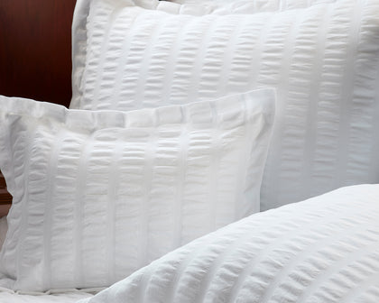 White seersucker-textured Panama shams and bedding on a bed with a dark wood headboard.