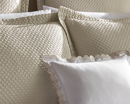 Textured cream Perla shams layered with a white scalloped-trim pillow on a bed.