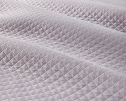Lavender diamond-quilted Petra coverlet draped on a bed.