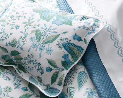 White Pomegranate floral-print pillow sham with blue and green botanicals layered with a quilted blue throw.